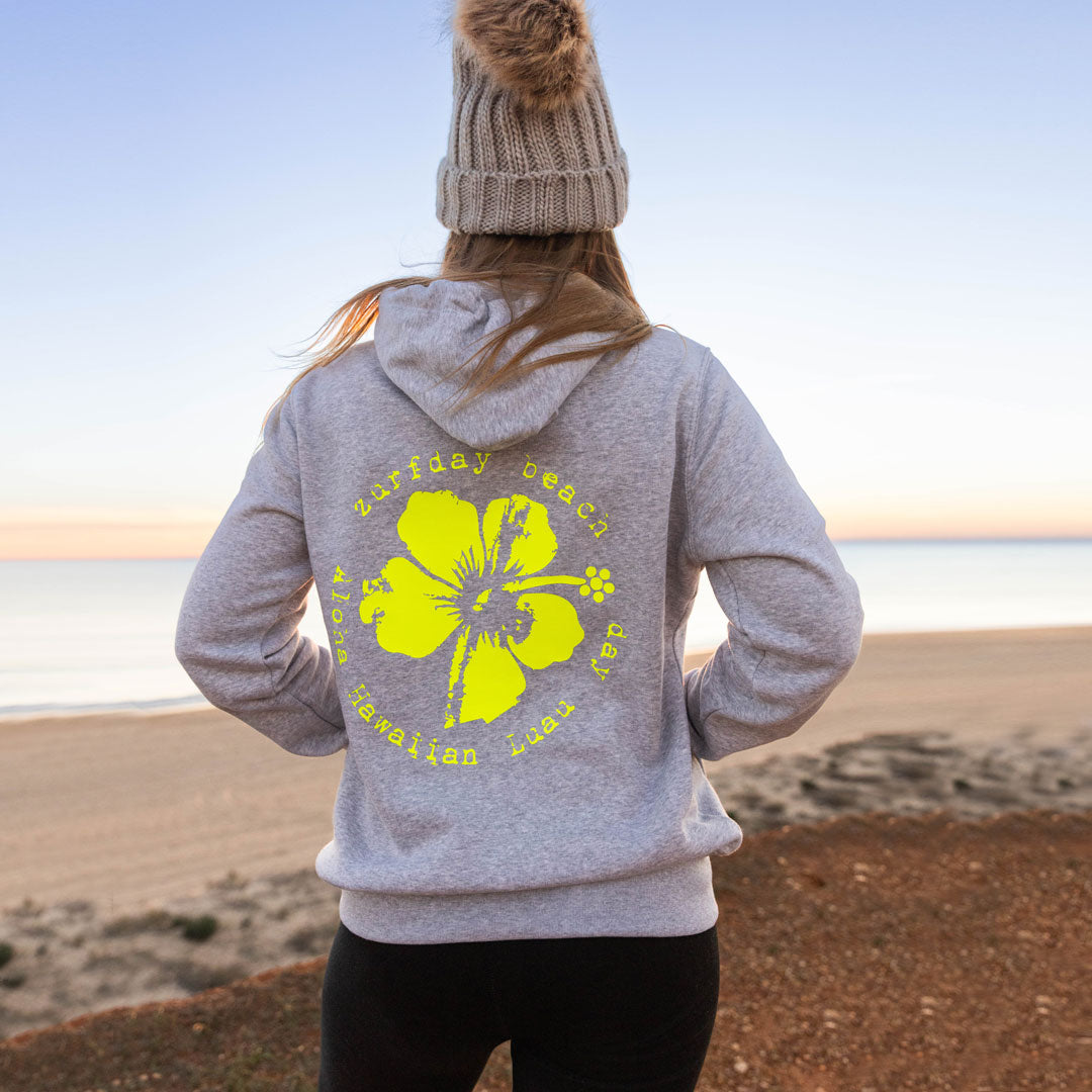Junge Frau am Strand schaut aufs Meer, sie trägt einen Zurfday Hoodie mit großem Blumen Motiv