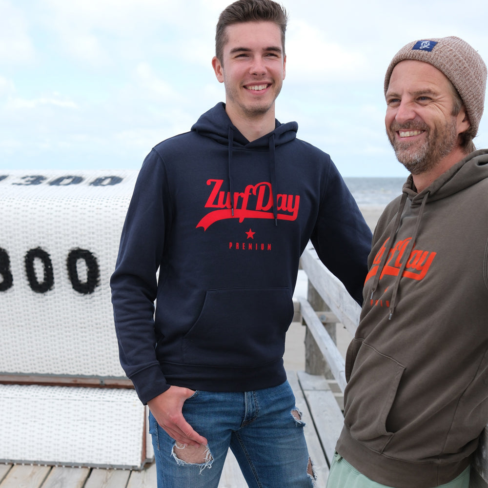 Zwei Freunde stehen am Strand, beide tragen einen Zurfday Hoodie, einmal in Navi und einmal in Olive