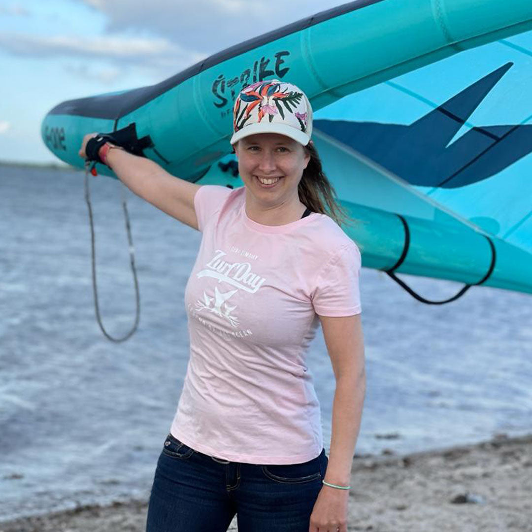 Sabrina steht am Strand, mit ihrem neuen Wing und trägt dabei ein rosanes Zurfday T-Shirt aus der SOS Kampage