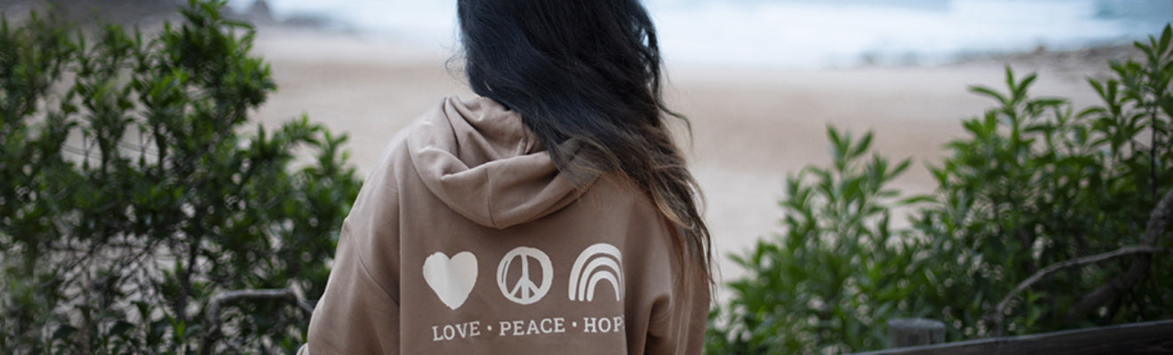 Eine junge Frau schaut auf den Strand und trägt einen Zurfday Hoodie mit der Aufschrift Love, Peace Hope