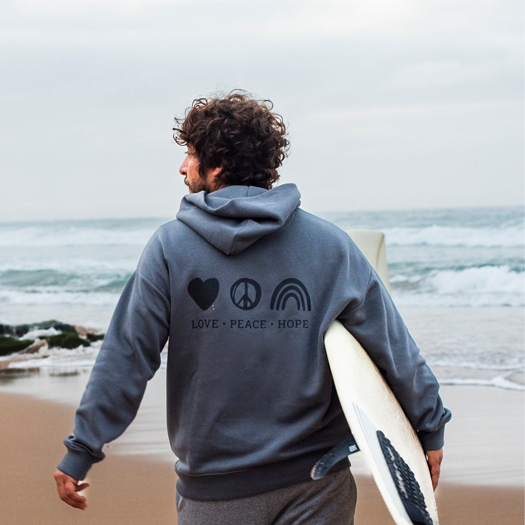 Junger Surfer mit Surfboard blickt aufs Meer und trägt einen grauen Zurfday Hoodie