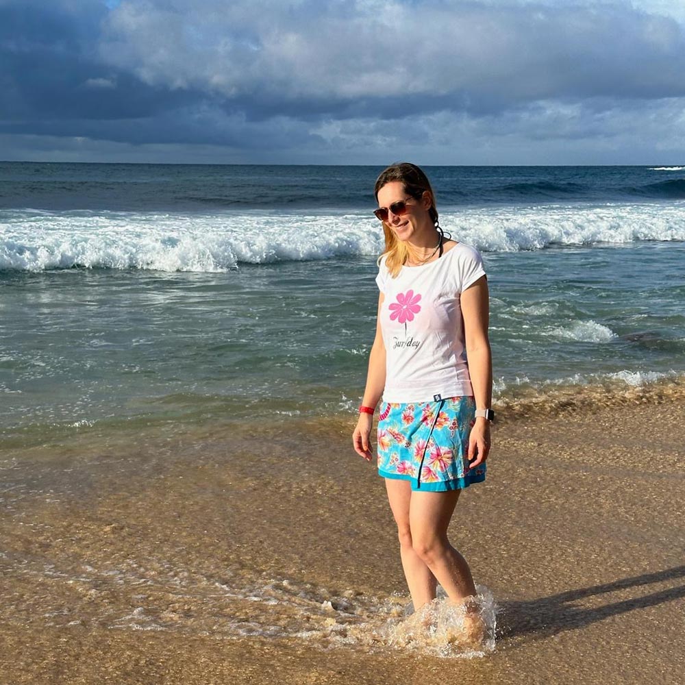 Eine junge Frau geht am Strand spazieren, sie trägt einen Zurfday Rock und lächelt vor sich hin