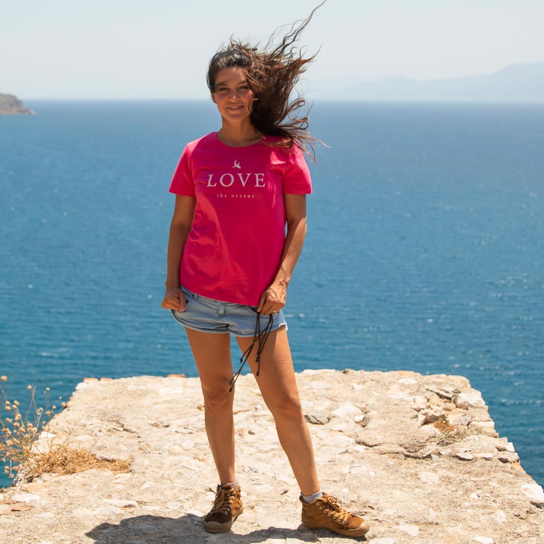 Eine junge Frau steht auf einem Felsen, vor dem Meer, sie trägt ein pinkes T-Shirt von Zurfday