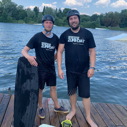 Timo und Ove stehen am Steg beim Wakeboarden und tragen ein Zurfday T-Shirt