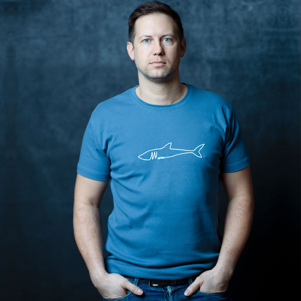 Benny trägt ein blaues T-Shirt mit einem weißen Zurfday Hai drauf.